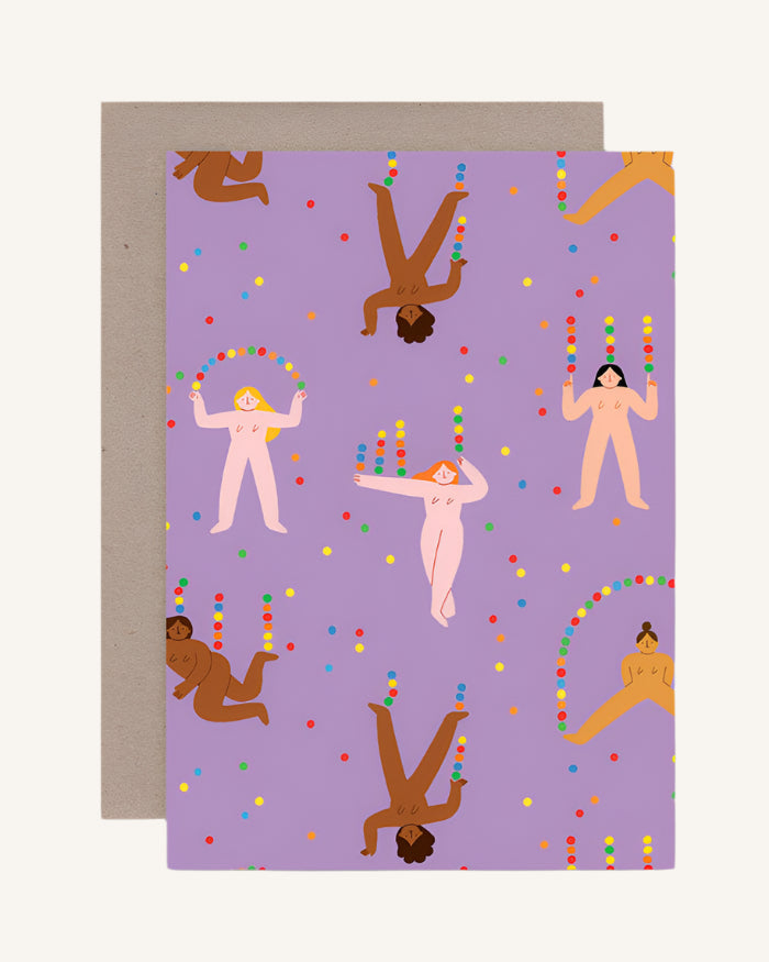 A colorful greeting card featuring illustrated jugglers and various objects being juggled, such as balls and pins, against a purple background. The card is shown with a blank inside and a brown envelope.